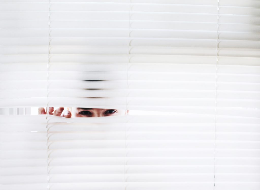 a woman peeking through window blinds