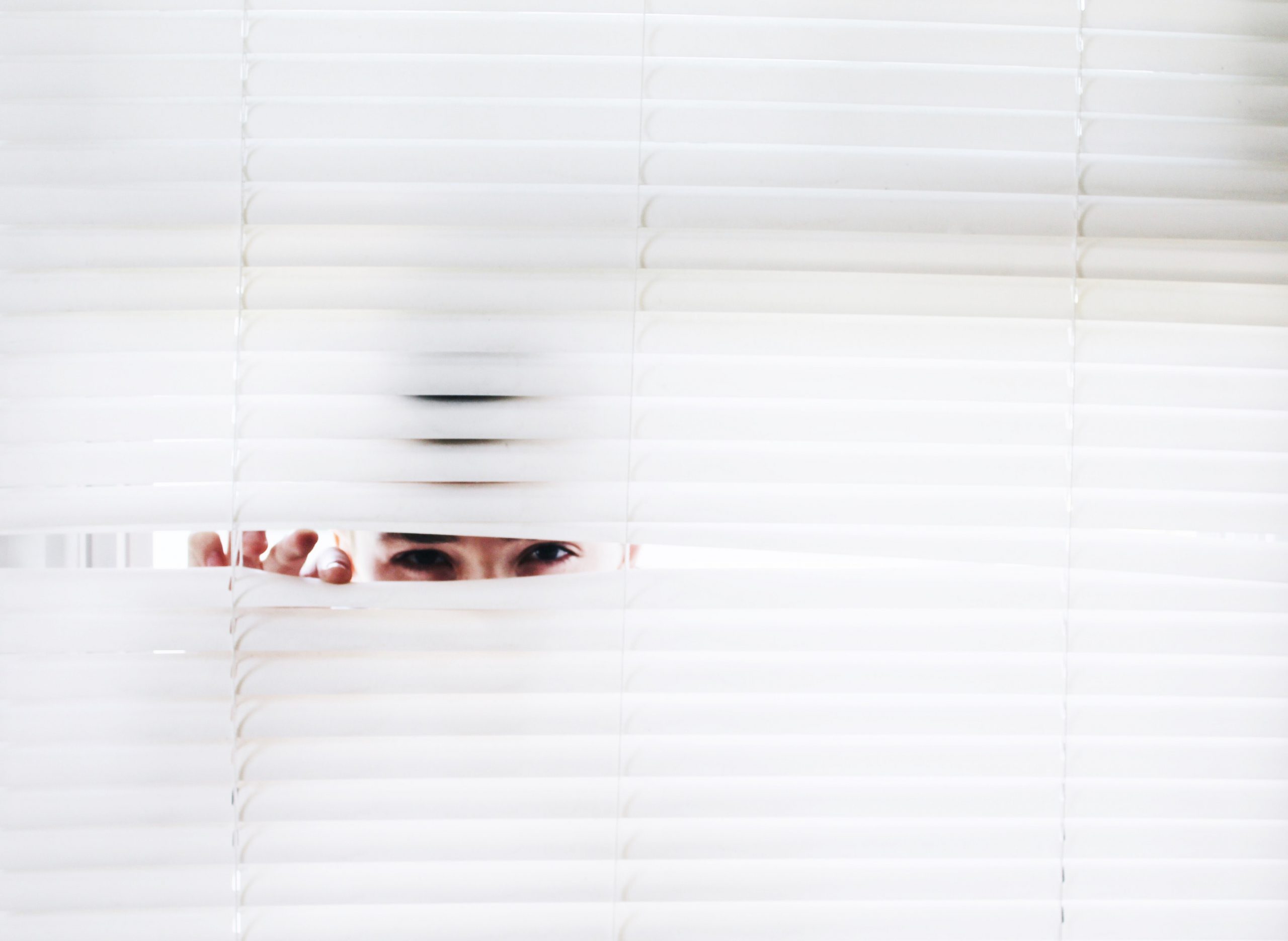 a woman peeking through window blinds