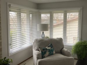 Corner windows with horizontal blinds behind a sofa chair