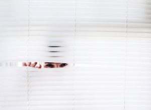 a woman peeking through window blinds