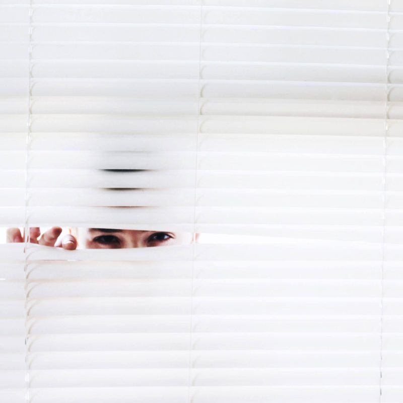 a woman peeking through window blinds