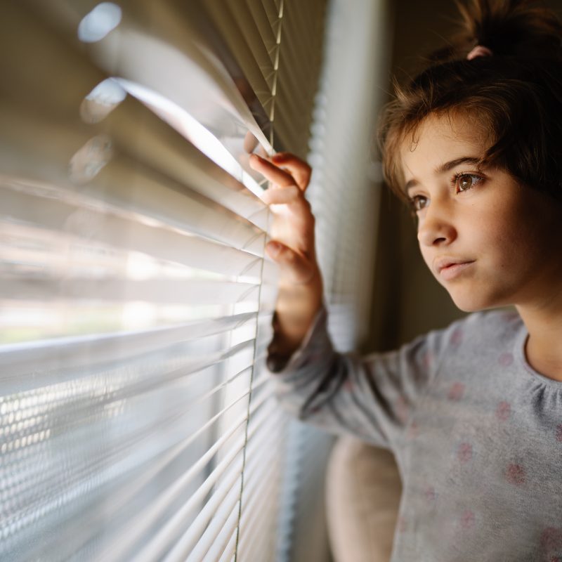 young girl looking through the blinds